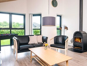 A modern living room with a sofa, two chairs, a coffee table, a foosball table, a fireplace, and large windows.