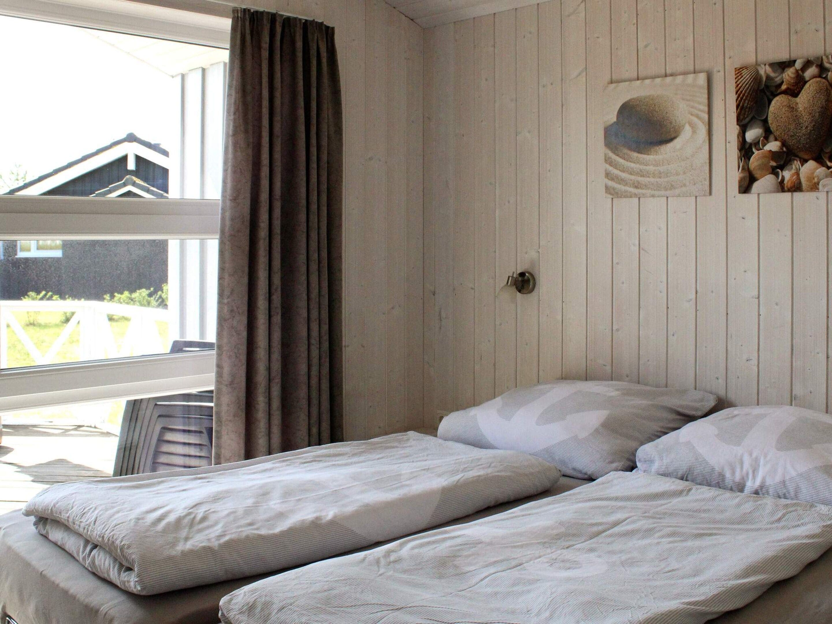 A room with two beds, a window with curtains, and a wall with a picture of seashells.
