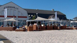 Un restaurante junto a la playa llamado Strandhalle, con mesas al aire libre y sombrillas.