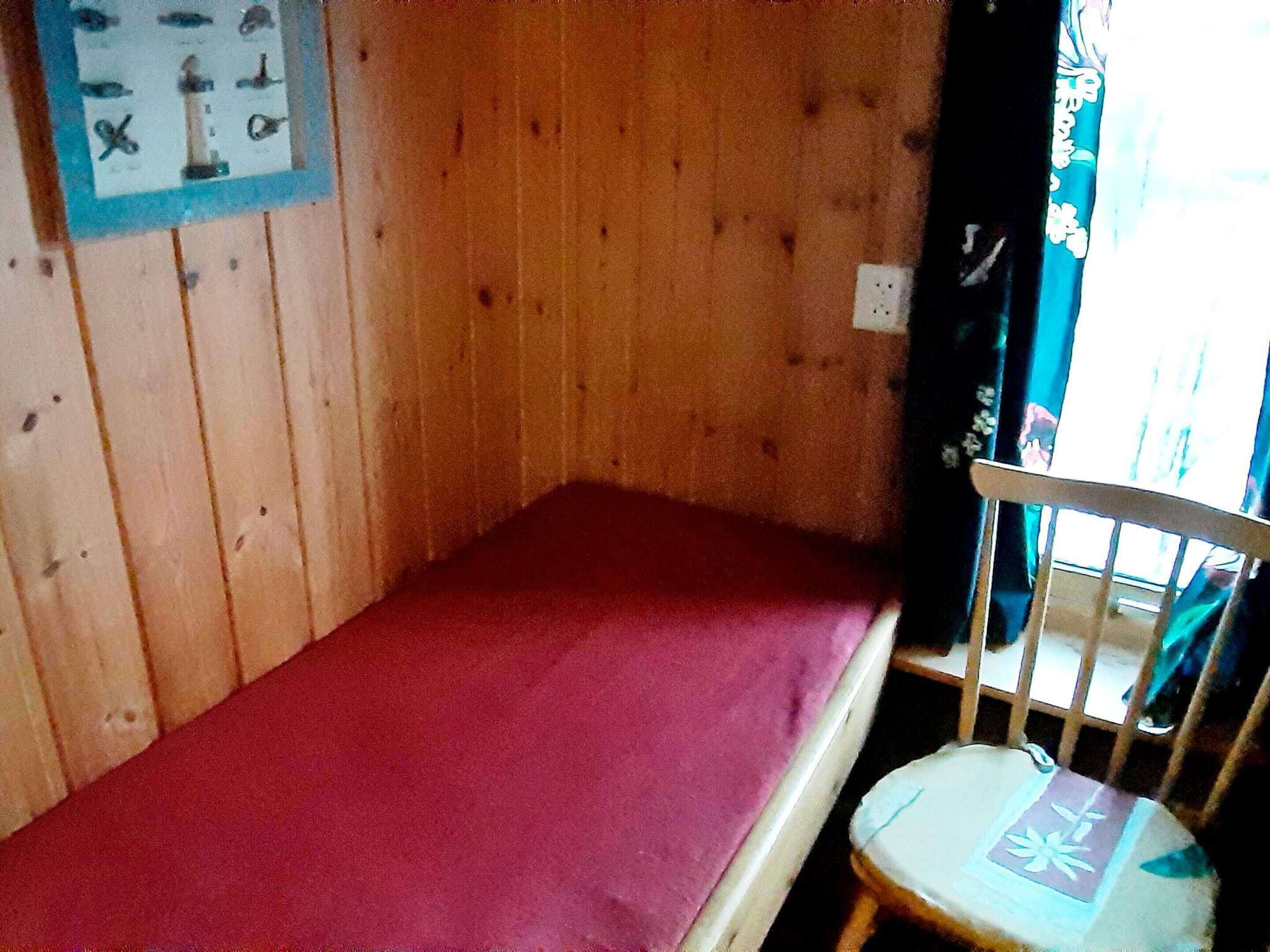 A small wooden room with a single bed and a chair.