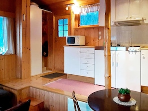 A wooden cabin interior with a kitchenette, a dining table with chairs, and a small potted plant.