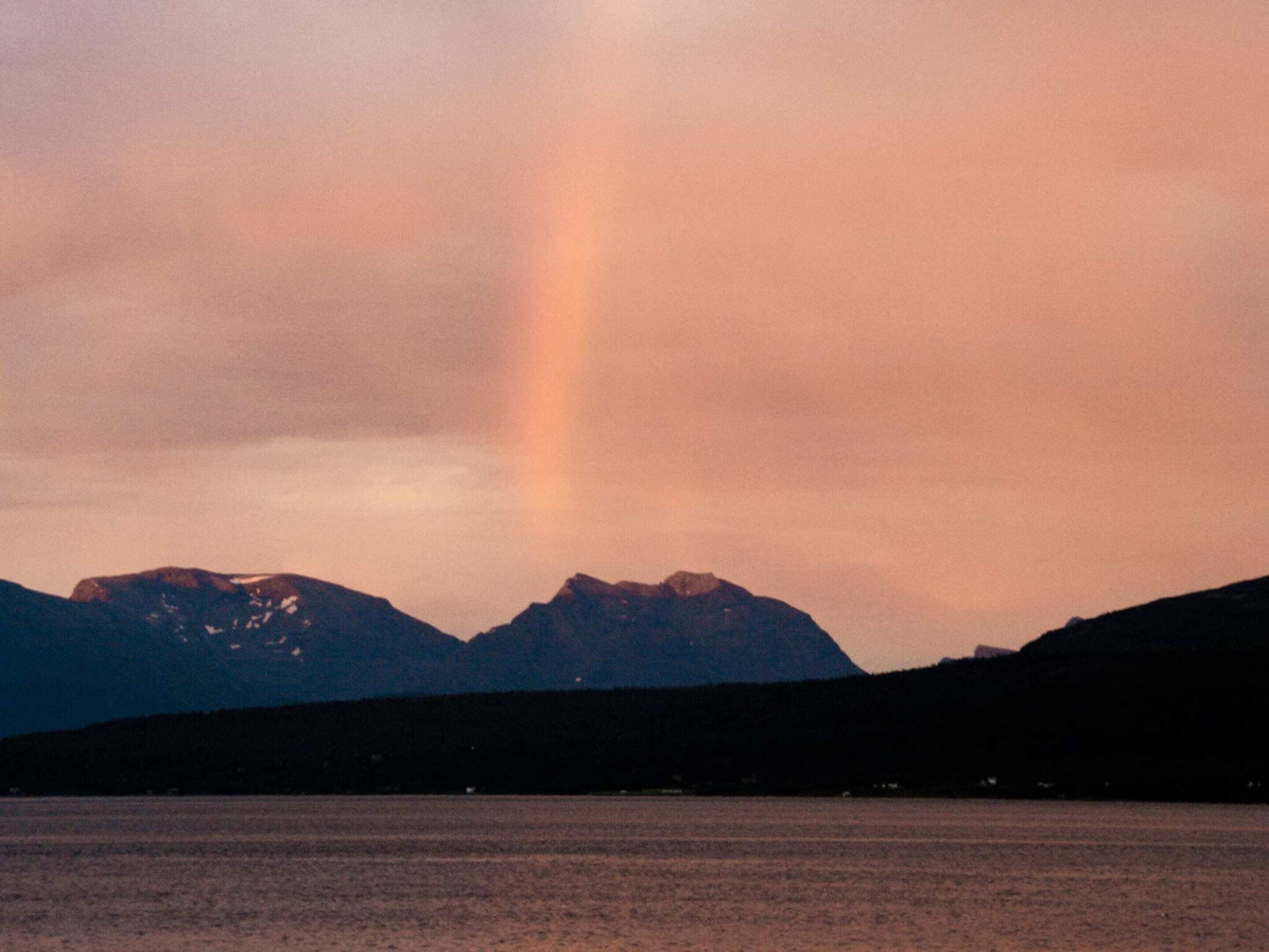 A mountain range with a visible rainbow over a body of water.