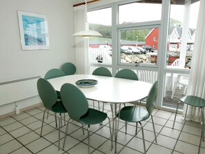 A dining area with a round table and six chairs, a window with a view of parked cars and houses, and a white radiator on the wall. - Quaint Holiday Home in Hasle near Sea (Hasle)