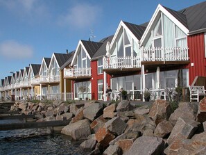 Eine Reihe von Ferienhäusern am Meer mit Balkonen, eine felsige Küstenlinie und ein klarer Himmel.