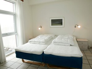 A double bed with a blue mattress and white bedding, two bedside tables, a wall-mounted lamp, and a framed picture on the wall.