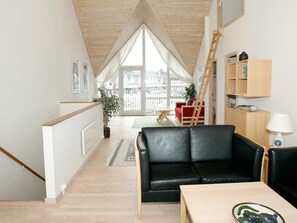 A modern interior with a black leather sofa, wooden flooring, a wooden ladder, and a view through large windows.