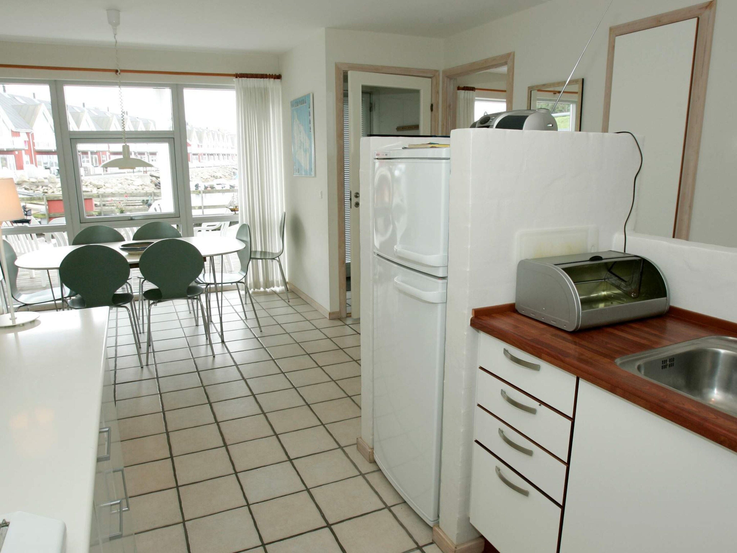 A compact kitchen with a refrigerator, a toaster, and a sink. There is a dining area with chairs and a table.