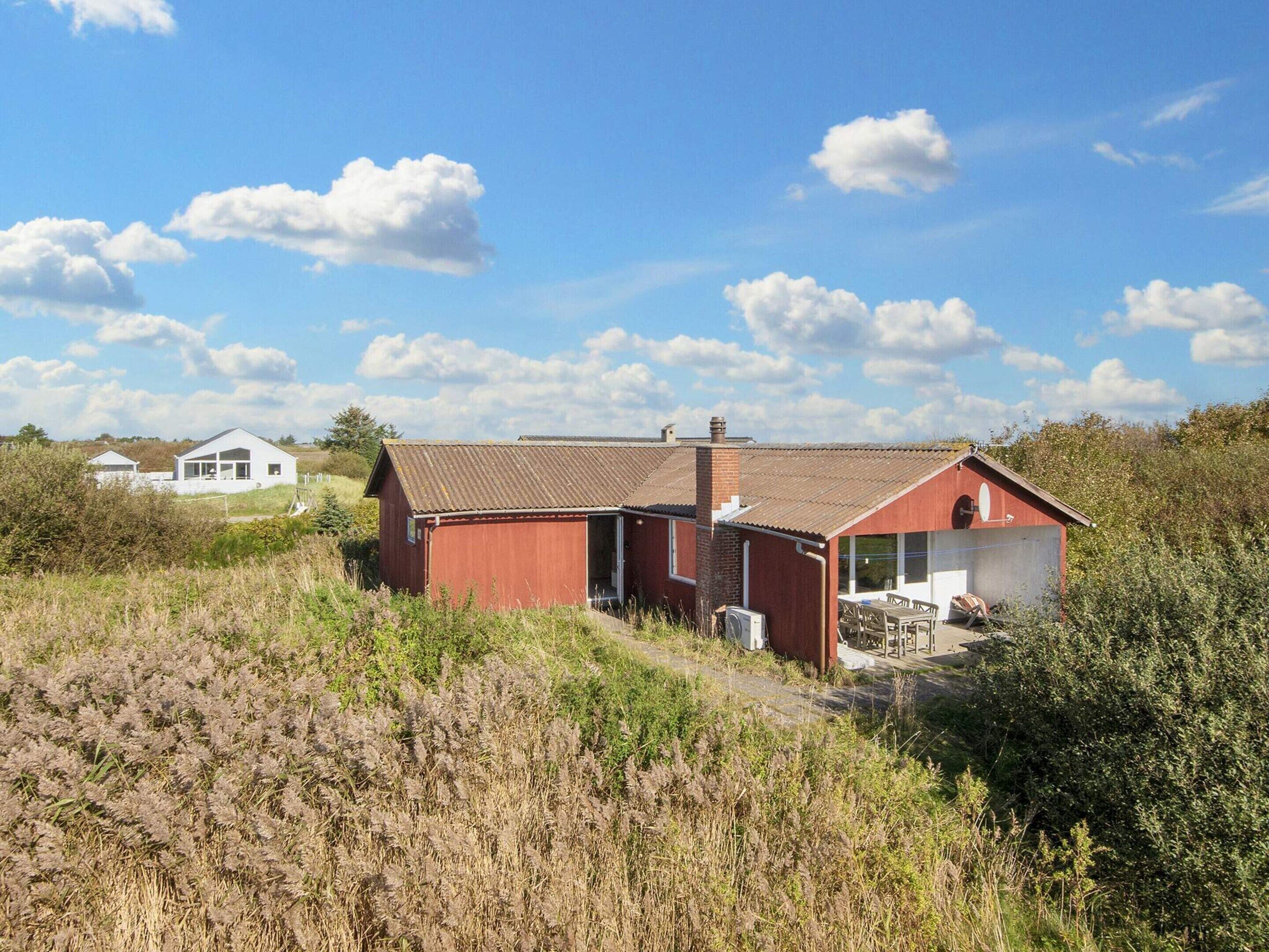 En röd byggnad med en skorsten, en vit byggnad i bakgrunden och en gräsklädd åker.