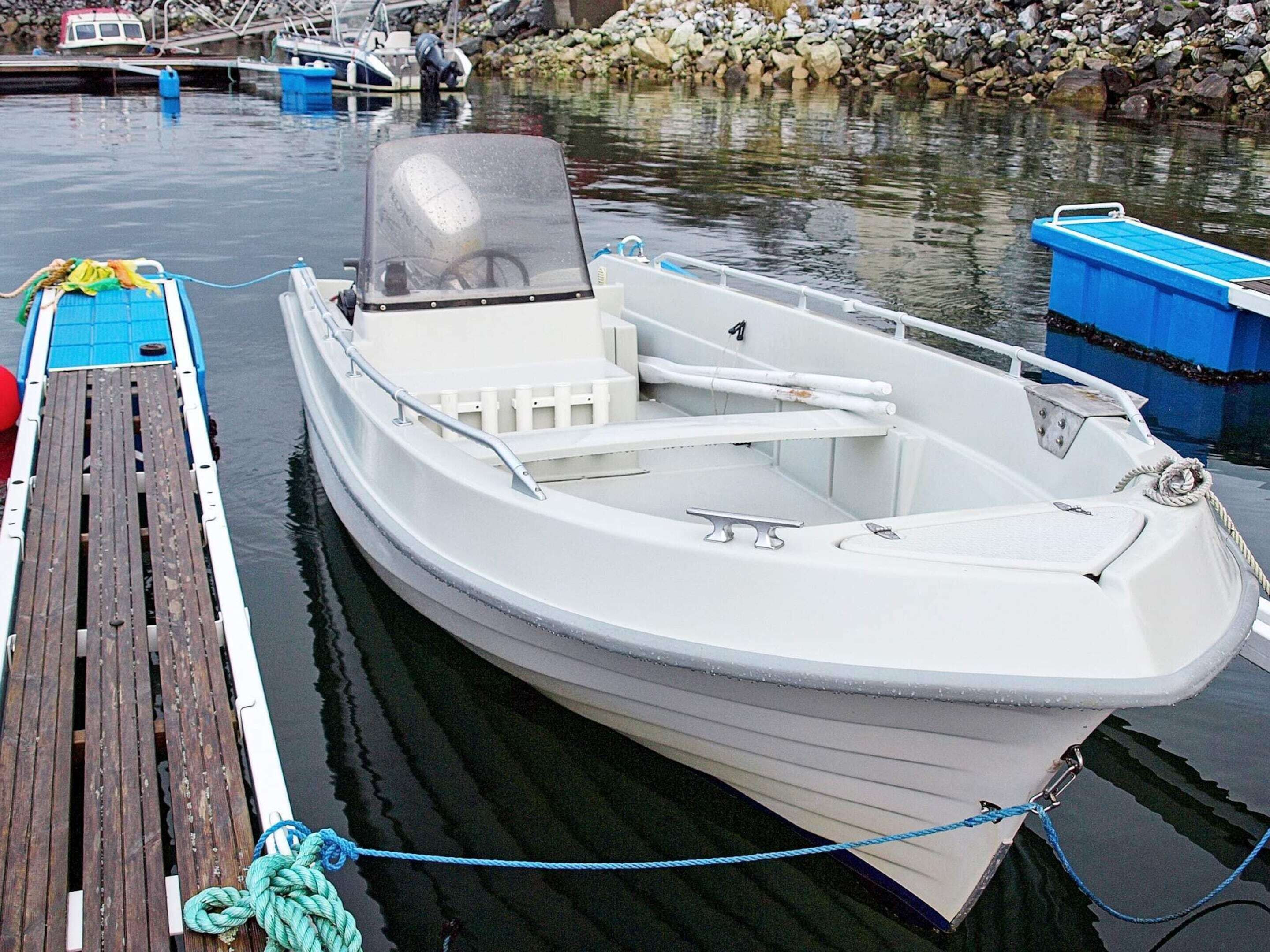 Una pequeña embarcación blanca amarrada en un muelle con cubierta de madera y una costa rocosa al fondo.