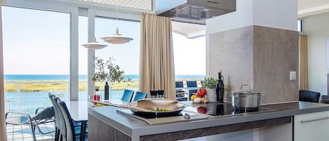 Una cocina moderna con una isla grande, un comedor con vistas al mar y un techo alto con tragaluces.