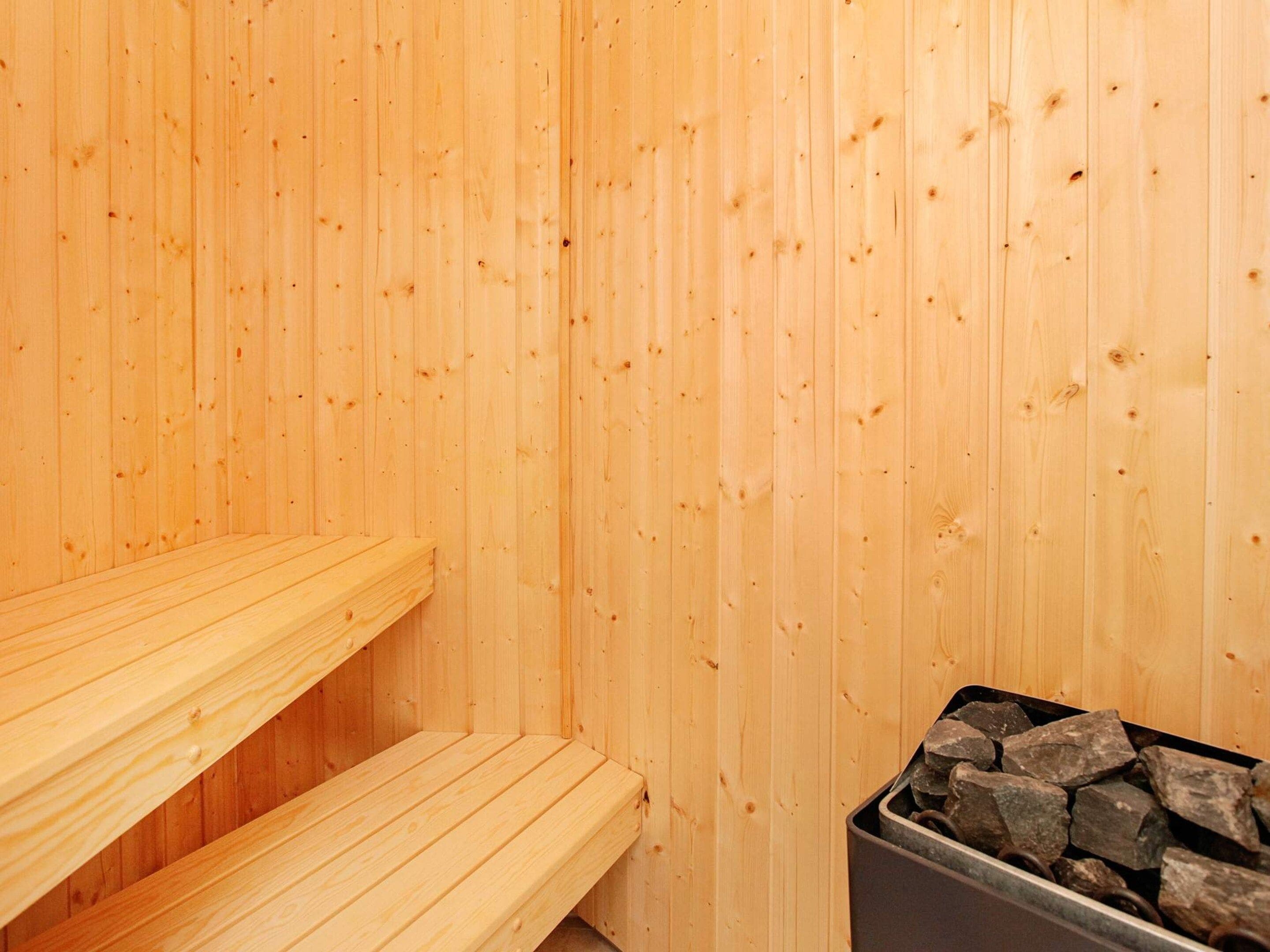 A wooden sauna with benches and a container of stones.