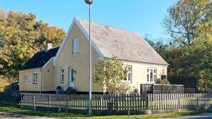 A two-story house with a gabled roof, a front porch, and a picket fence.