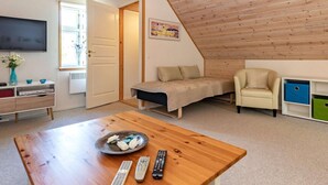 A cozy loft bedroom with a sloped ceiling, a bed, a sofa, and a TV.