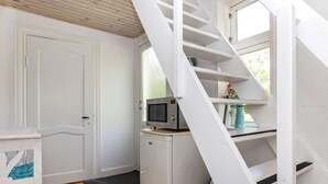 A compact room with a white door, a small white cabinet with a microwave, a black broom, and a blue vase on a shelf.
