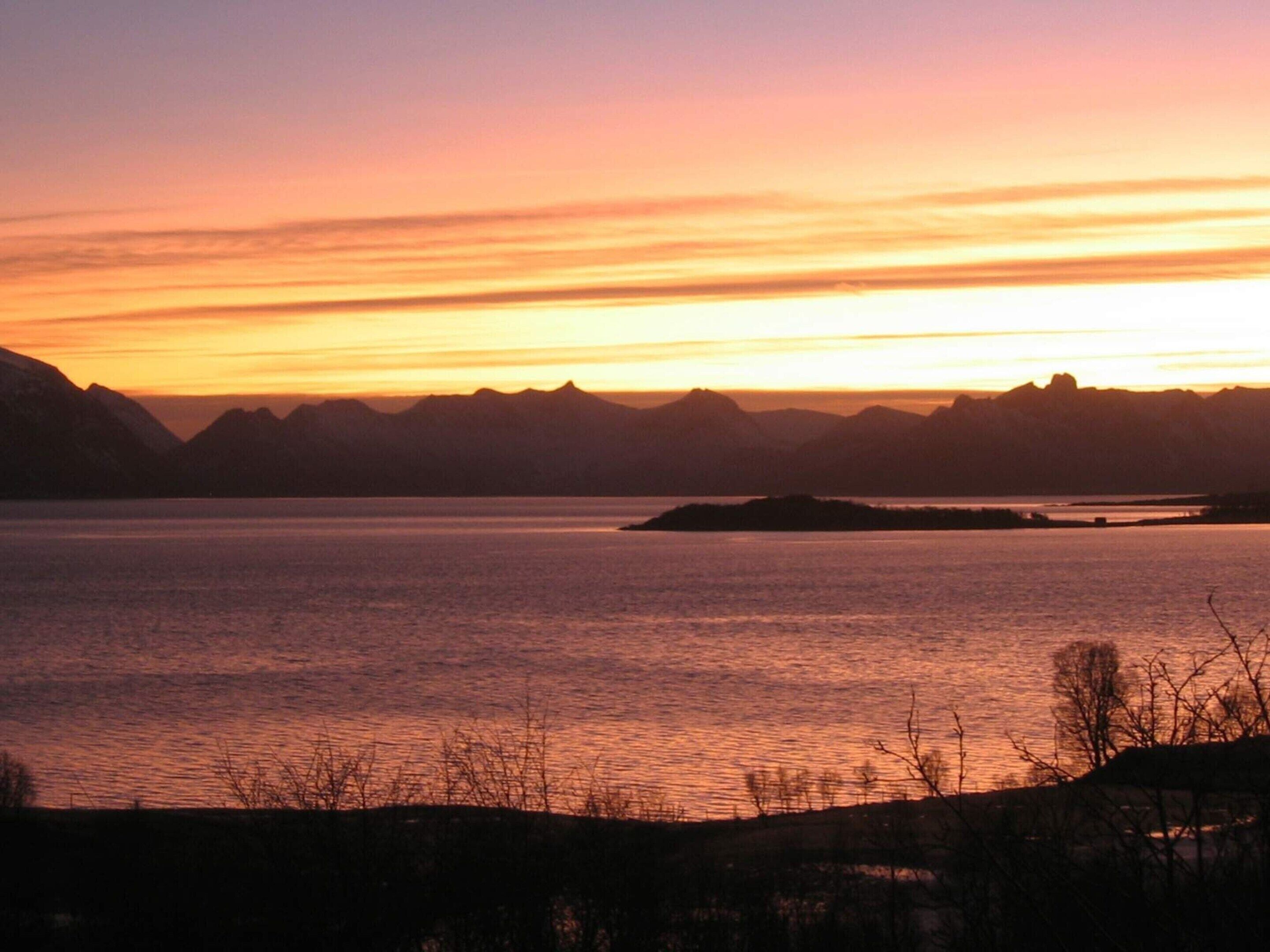 A sunset over a calm lake with mountains in the background.