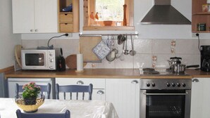A compact kitchen with white cabinets, a microwave, an oven, and a window with a view of greenery. - 6 Person Holiday Home in Alsvag-by Traum (Oksnes)