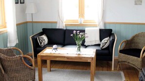 A living room with a sofa, two wicker chairs, a wooden coffee table, and a vase with flowers. - 6 Person Holiday Home in Alsvag-by Traum (Oksnes)