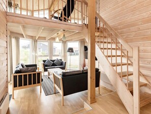 A wooden interior with a staircase, a sofa, a table, and a view of the outdoors.