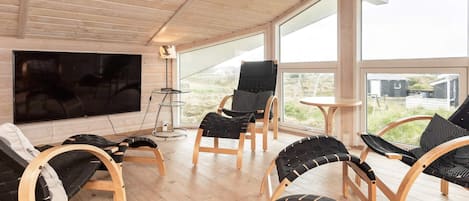 Een modern interieur met houten vloeren, een flatscreen televisie en meerdere zwarte fauteuils.