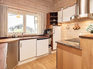 A modern kitchen with wooden cabinetry, a built-in dishwasher, a coffee machine, and a stainless steel range hood. - 5 Star Holiday Home in Thisted (Thisted)