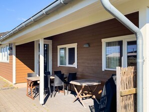 A wooden house with a covered patio, outdoor seating, and a visible window.