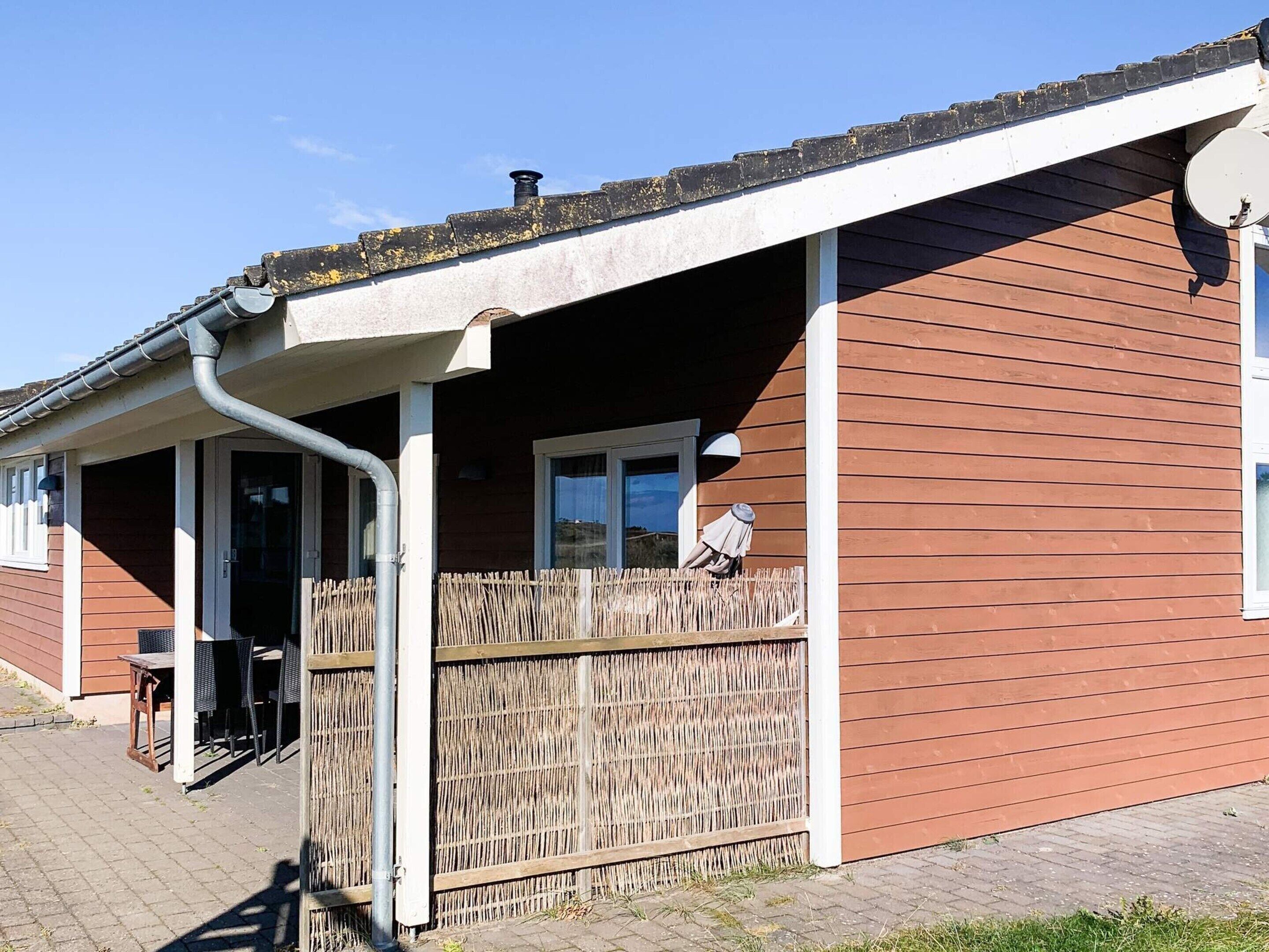 A single-story building with a covered patio area, a wooden fence, and a satellite dish.