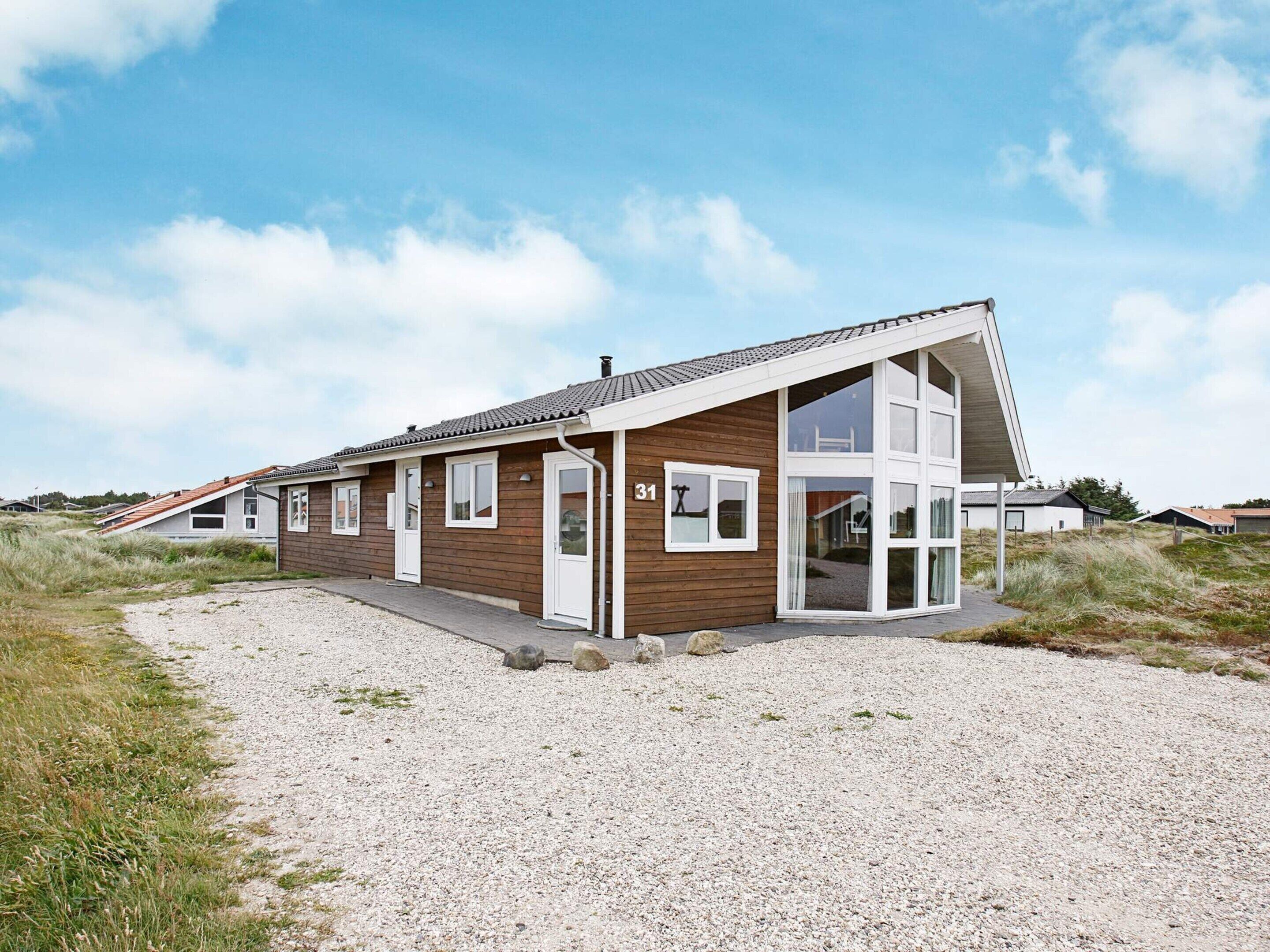 A modern, single-story building with a sloped roof, large windows, and a gravel driveway.