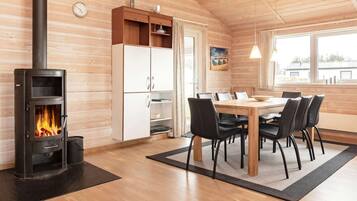 Una habitación acogedora con estufa de leña, una mesa de comedor con sillas y un ventanal grande.
