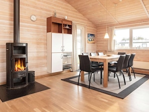 A cozy room with a wood-burning stove, a dining table with chairs, and a large window. - 5 Star Holiday Home in Thisted (Thisted)
