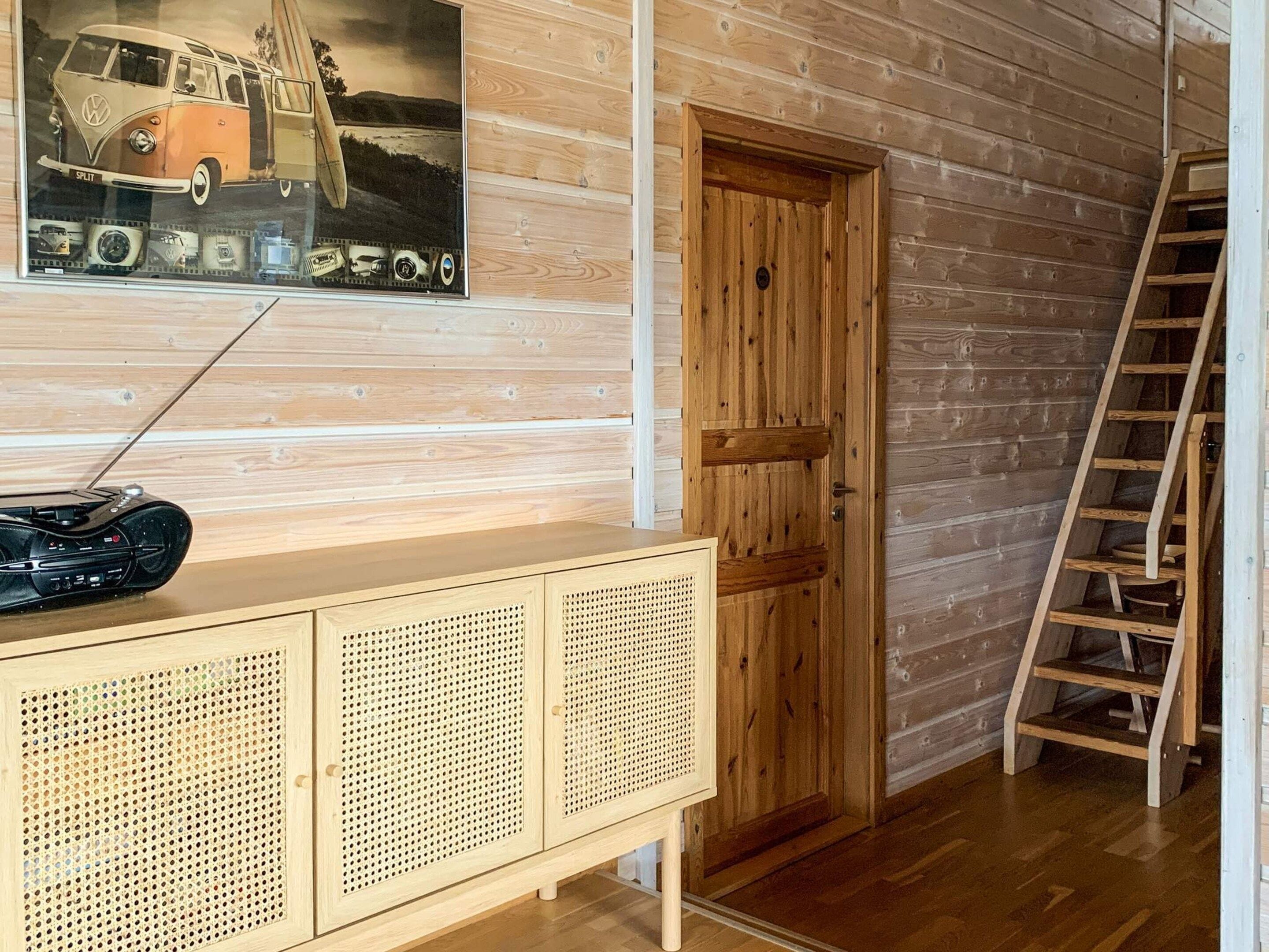 A wooden cabin interior with a wooden door, a wooden cabinet with perforated panels, and a ladder against the wall.