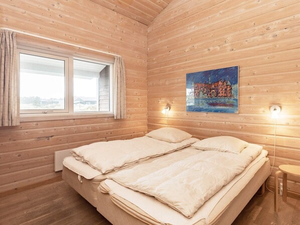 A wooden cabin room with a bed, a window, and a painting on the wall.