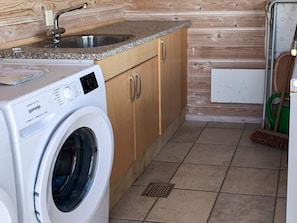 A compact kitchen with a washing machine, wooden cabinets, a granite countertop, and a green cleaning tool. - 5 Star Holiday Home in Thisted (Thisted)