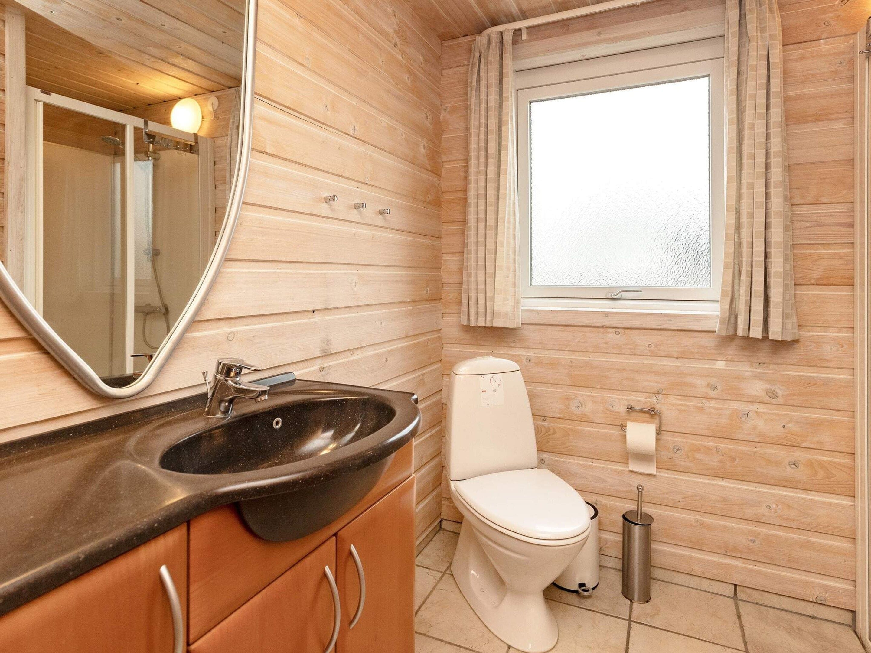 A compact bathroom with a wooden interior, a sink, a toilet, and a window with curtains.