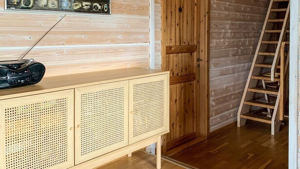 Interior em madeira com porta de madeira, escada, armário com painéis perfurados e um rádio em cima.