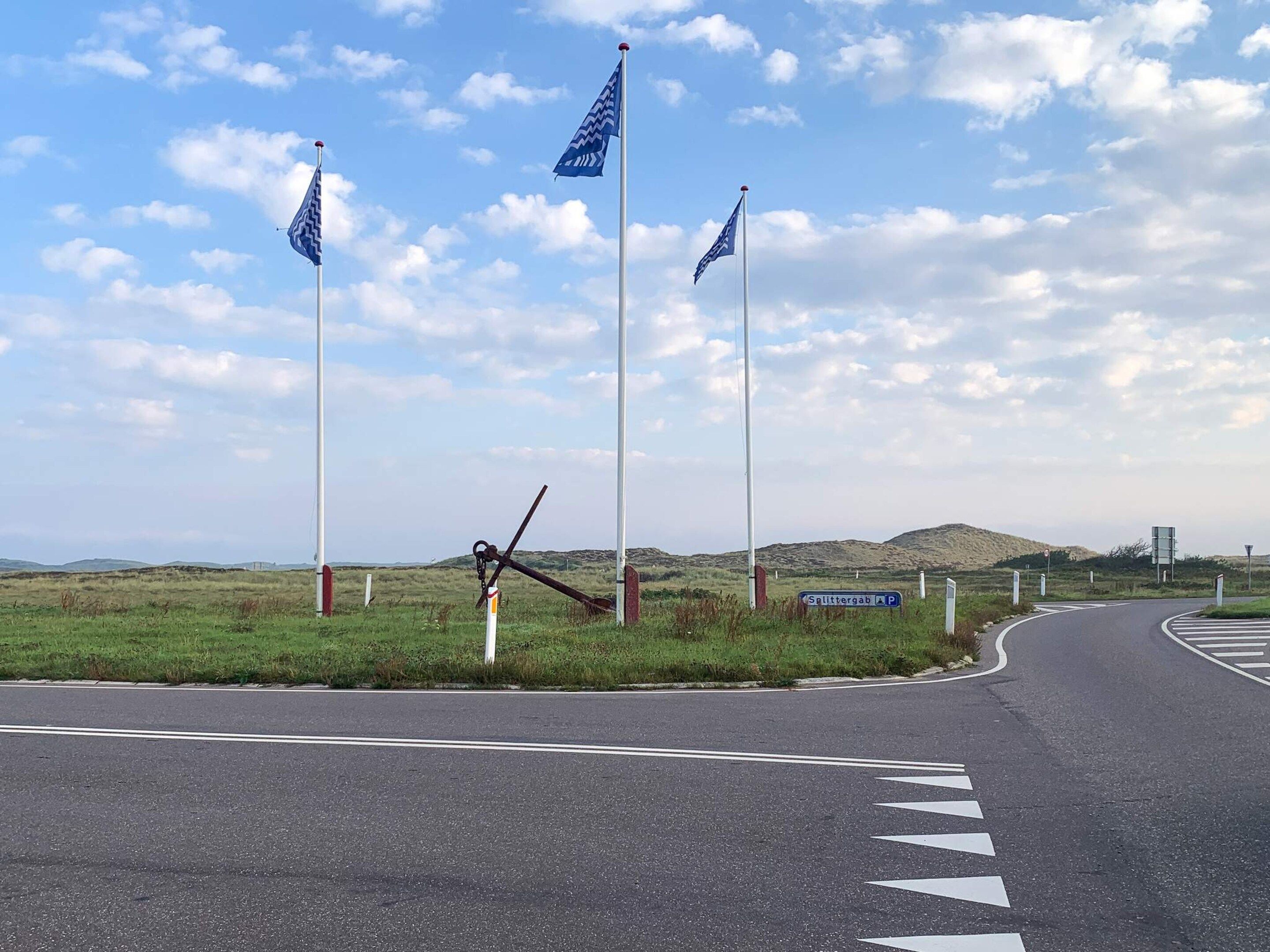 Une route avec un panneau indiquant « Splittergab P » et trois drapeaux sur des mâts.