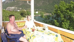 Un espacio al aire libre techado con una mesa lista para dos personas, con vista a un lago y montañas.
