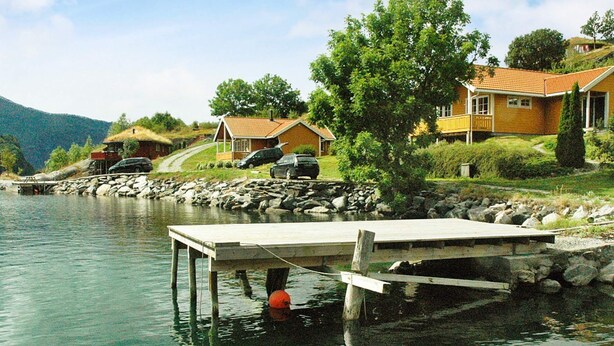 Una propiedad frente al lago con un muelle que se adentra en aguas tranquilas, rodeada de casas y vegetación.