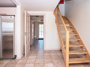 A kitchen with a stainless steel refrigerator, a wooden staircase, and a hallway leading to a door.