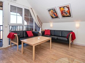 A modern living room with a black leather sofa, a wooden coffee table, and two abstract paintings on the wall.