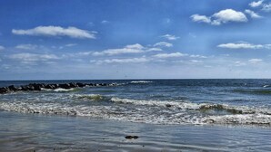 Una spiaggia con onde, cielo sereno e un litorale roccioso.