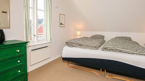 Una camera da letto con un letto, una cassettiera, una finestra con tende, un termosifone e una lampada a parete.