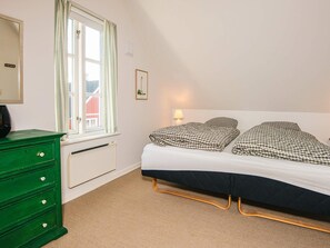 A bedroom with a bed, a dresser, a window with curtains, a radiator, and a wall-mounted lamp. - 5 Star Holiday Home in Blavand (Blavand)