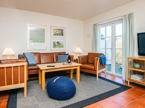 A living room with a brown leather sofa, a wooden coffee table, and a blue bean bag. There are two lamps, a television on a wooden stand, and framed artwork on the wall. - 5 Star Holiday Home in Blavand (Blavand)