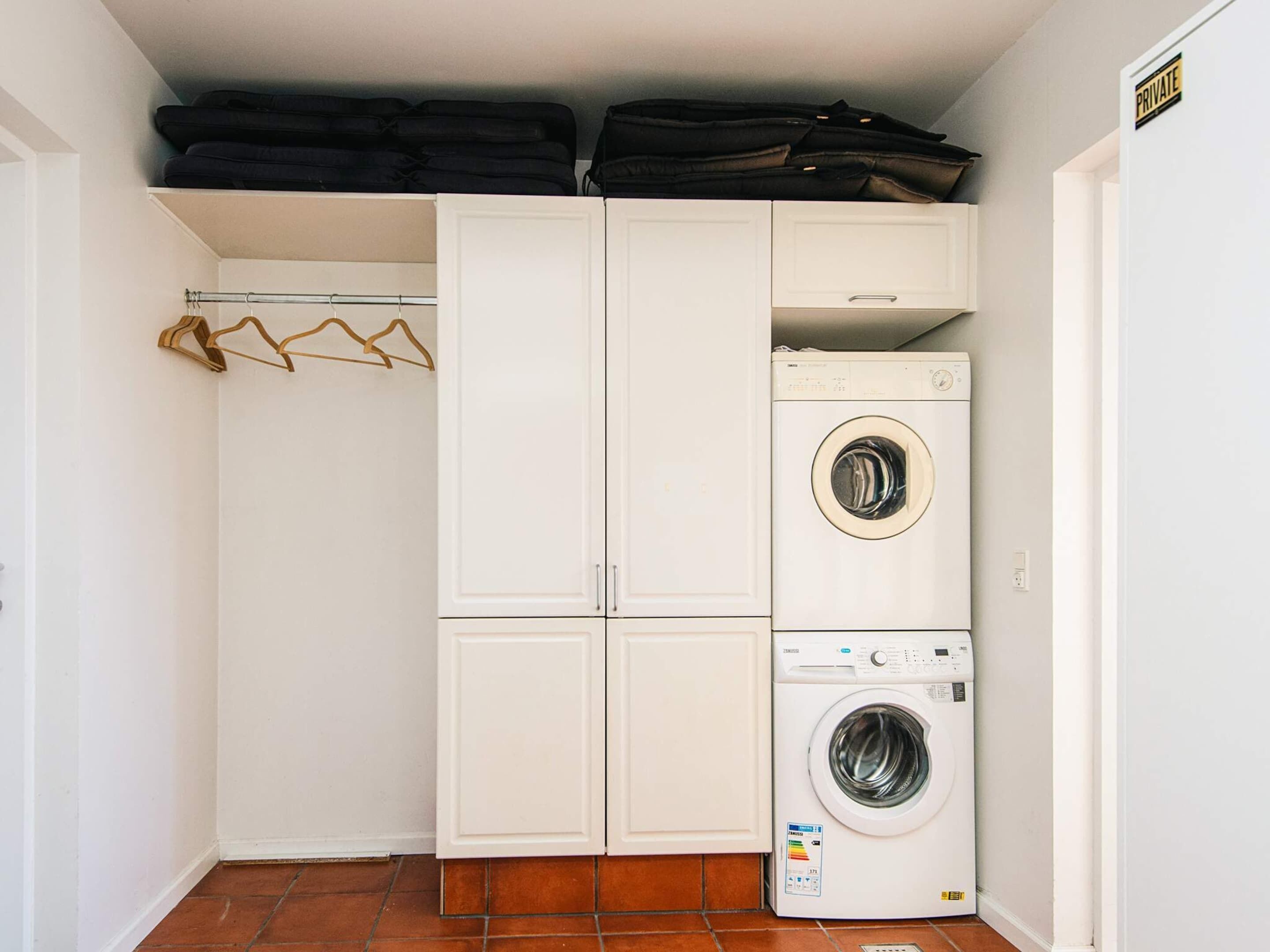 Une buanderie équipée d’un lave-linge et d’un sèche-linge superposés, d’un étendoir et d’une pancarte indiquant qu’elle est réservée à un usage privé.