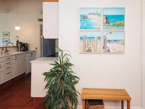 A modern kitchen with white cabinets, a sink, and a coffee maker. There is a wooden bench and a potted plant in the center. - 5 Star Holiday Home in Blavand (Blavand)