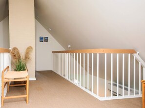 A room with a wooden chair, a white railing, and a wall-mounted lamp.