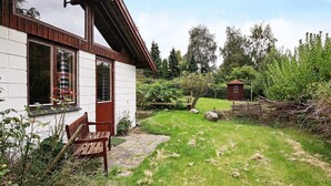 A rustic house with a wooden bench outside, a small shed, and a grassy yard with a wooden fence. - Holiday Home in Nykøbing Sjælland near Sea (Nykobing Sjaelland)