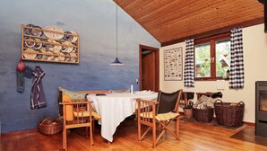 A cozy room with a wooden ceiling, a table with chairs, a wall-mounted plate rack, a window with checkered curtains, and a fireplace. - Holiday Home in Nykøbing Sjælland near Sea (Nykobing Sjaelland)