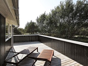 A wooden deck with a bench and a railing, surrounded by trees.