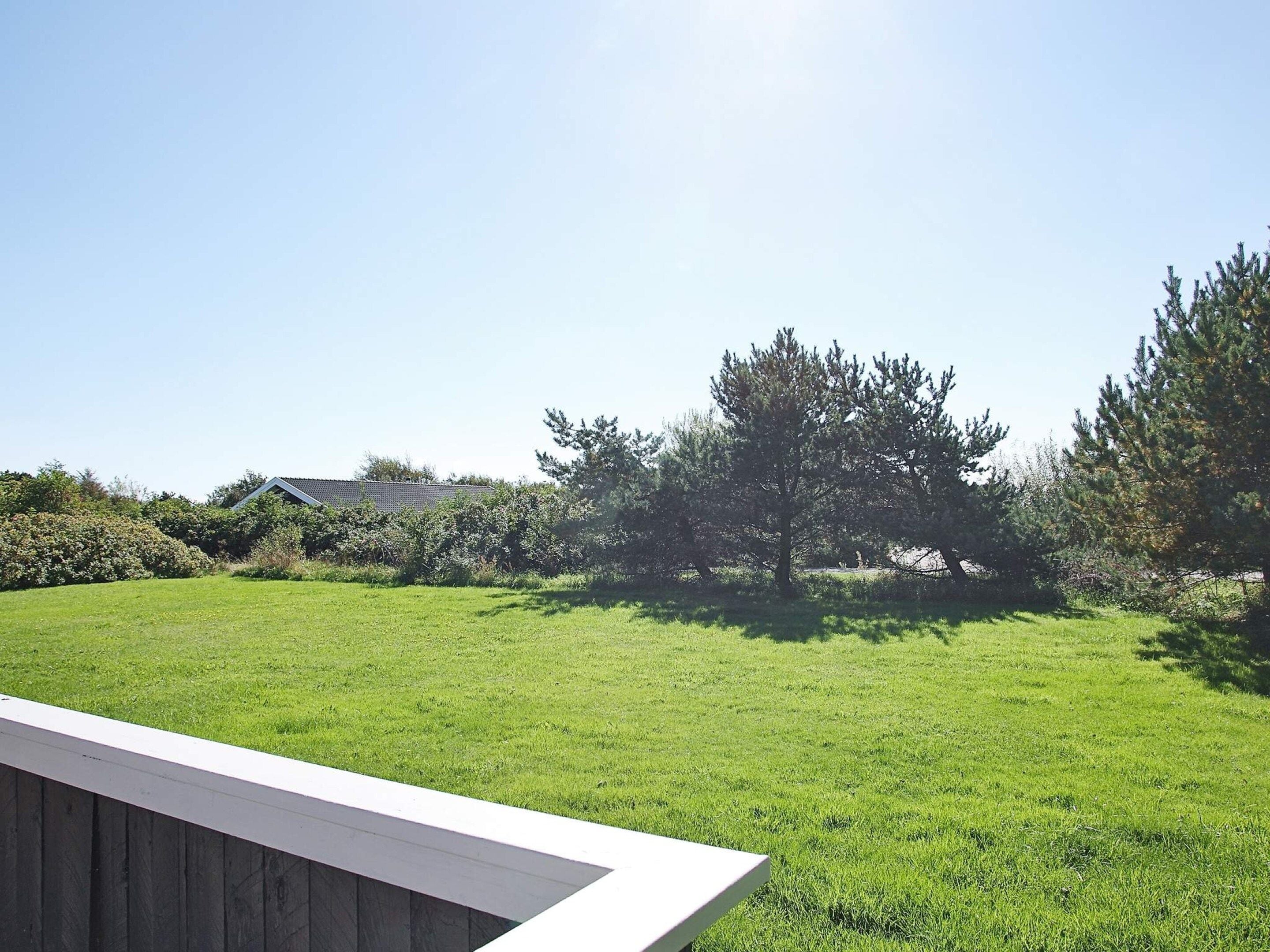 A grassy outdoor area with a wooden deck in the foreground and trees in the background.